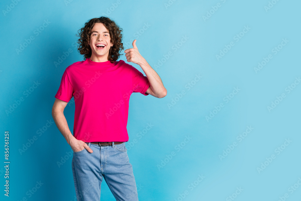 Photo of nice young man show thumb up empty space wear pink t-shirt isolated on blue color background Photo of nice young man show thumb up empty space wear pink t-shirt isolated on blue color background