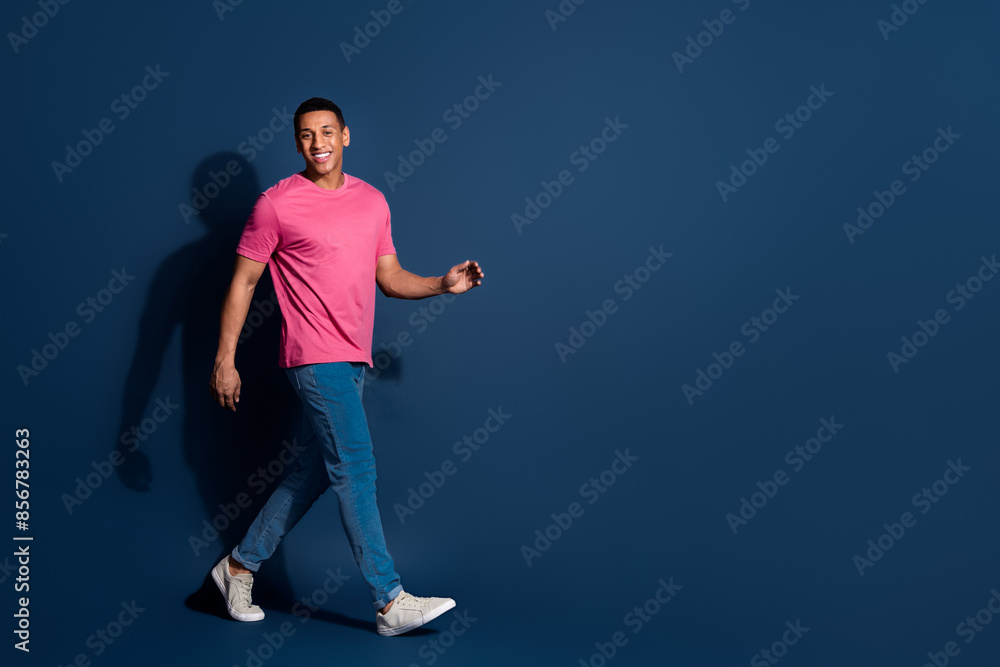 Full length photo of young funny guy wearing casual pink t shirt and jeans enjoying his brand new look isolated on dark blue color background Full length photo of young funny guy wearing casual pink t shirt and jeans enjoying his brand new look isolated on dark blue color background