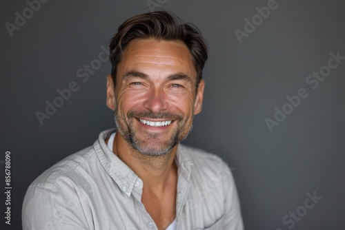 Portrait of a tender man in his 40s smiling at the camera in front of blank studio backdrop