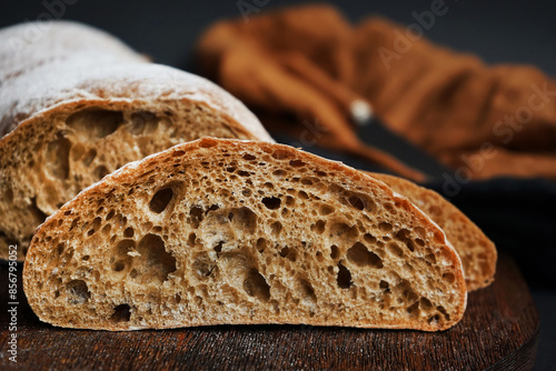 Fresh sliced ​​bread on a wooden board next to a knife with a linen napkin on a dark background
