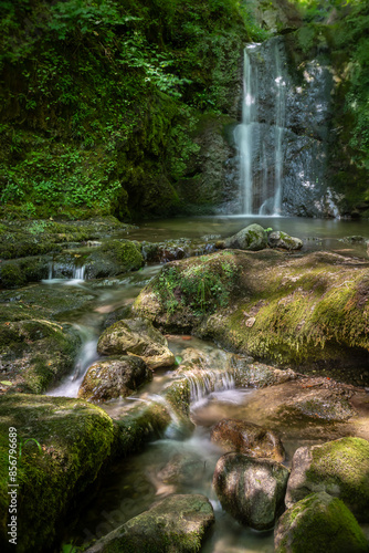 A tranquil waterfall cascades over moss-covered rocks in a lush green forest at Klaus an der Pyrhnbahn, Austria