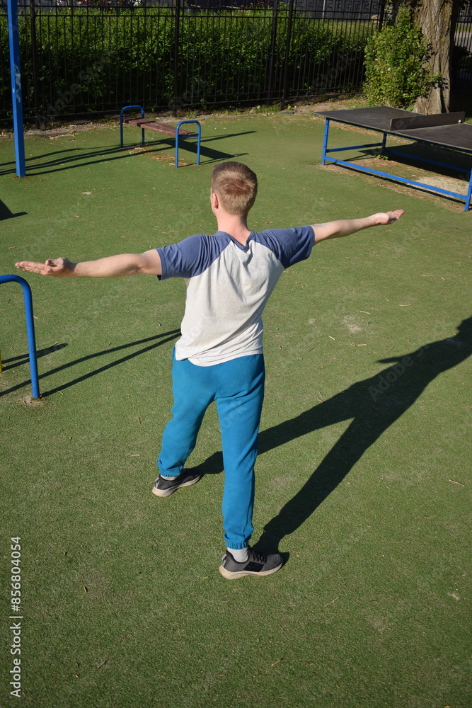 Obraz premium A focused young athlete dynamically performing warm-up drills and stretches outdoors. Clad in athletic gear, he meticulously prepares body for the physical demands ahead through a regimented routine