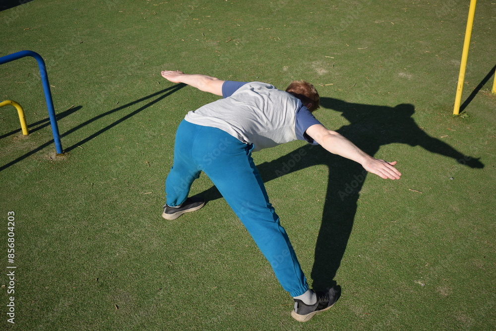Obraz premium A focused young athlete dynamically performing warm-up drills and stretches outdoors. Clad in athletic gear, he meticulously prepares body for the physical demands ahead through a regimented routine