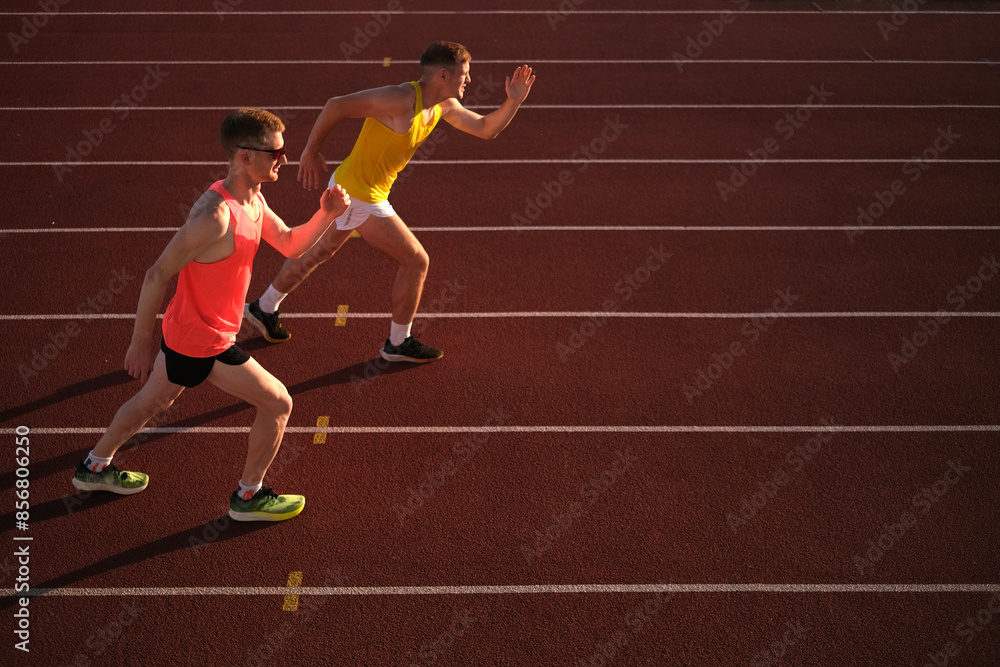 Two athletes running in a stadium at sunset