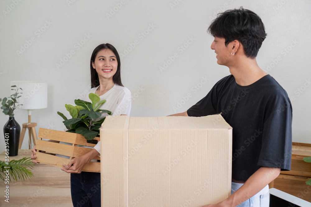 Young Couple Moving into New House, Carrying Boxes and Plants, Starting Fresh in Modern Home Young Couple Moving into New House, Carrying Boxes and Plants, Starting Fresh in Modern Home