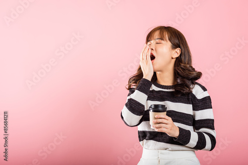 Portrait Asian beautiful happy young woman tired sleepy her cannot wake up and closes eyes holds take away cup coffee, studio shot isolated on pink background, with copy space, coffee not help you