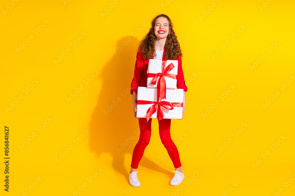 Full body portrait of gorgeous young lady hold pile stack giftbox wear red suit isolated on yellow color background Full body portrait of gorgeous young lady hold pile stack giftbox wear red suit isolated on yellow color background