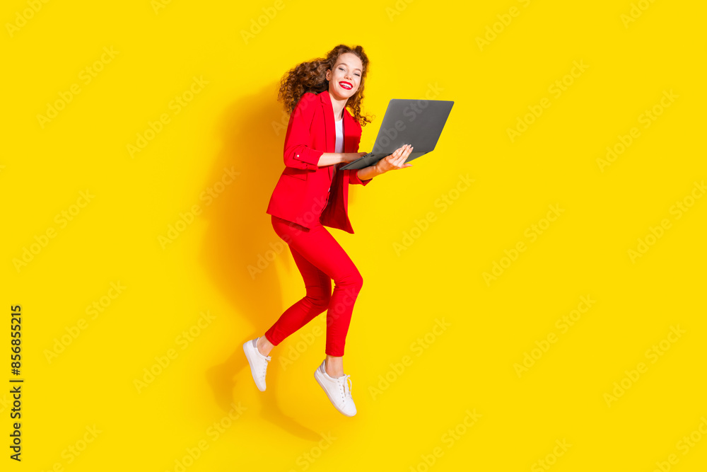 Full body portrait of gorgeous young lady jump use netbook wear red suit isolated on yellow color background Full body portrait of gorgeous young lady jump use netbook wear red suit isolated on yellow color background