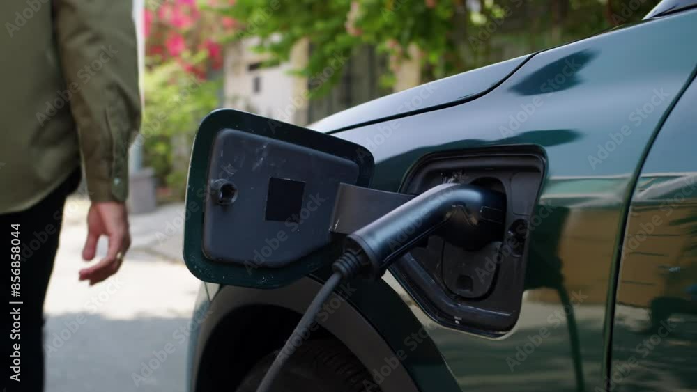 Handheld shot of male entrepreneur putting cable in charging port of electric automobile and leaving Handheld shot of male entrepreneur putting cable in charging port of electric automobile and leaving