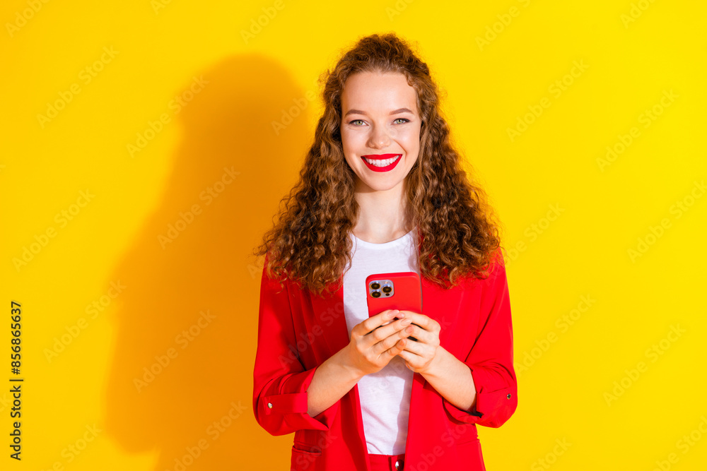 Portrait of gorgeous young lady hold smart phone empty space wear red suit isolated on yellow color background Portrait of gorgeous young lady hold smart phone empty space wear red suit isolated on yellow color background