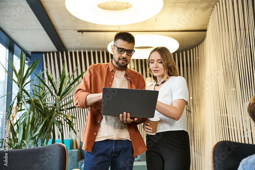 A man and a woman, colleagues in a coworking space, engaged in discussions while looking at a laptop screen. photo