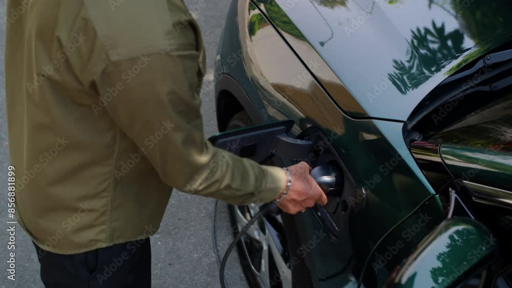 High angle view of unrecognizable man plugging charging cable in port of electric vehicle outdoors, concept of environmental awareness High angle view of unrecognizable man plugging charging cable in port of electric vehicle outdoors, concept of environmental awareness
