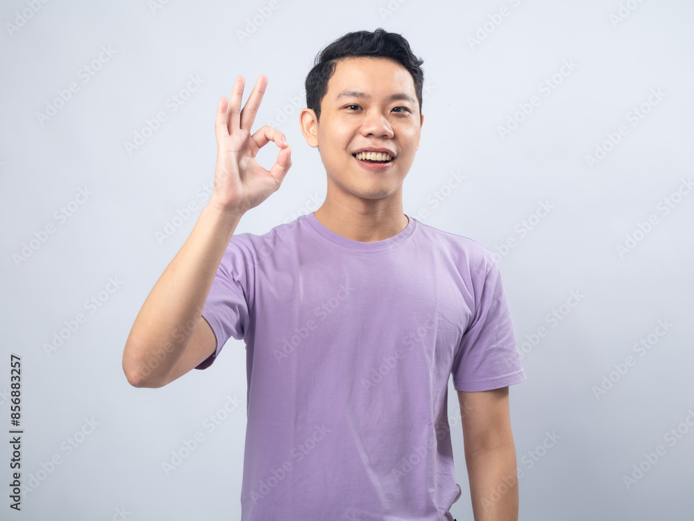 Young Asian man in a lavender t-shirt smiling and showing an Young Asian man in a lavender t-shirt smiling and showing an