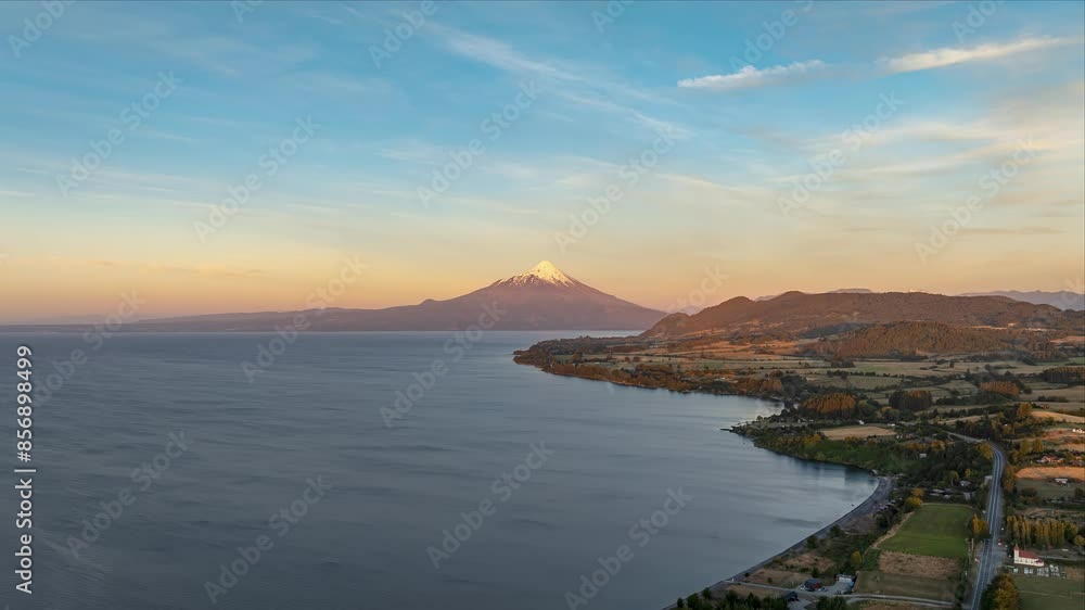 A serene aerial shot captures a vast lake with a snow-capped Osorno Volcano in the distance at sunset. Push Forward Shot A serene aerial shot captures a vast lake with a snow-capped Osorno Volcano in the distance at sunset. Push Forward Shot