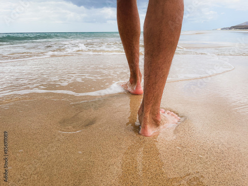 Stopy mężczyzny chodzącego po piasku i falach morskich. Mężczyzna spacerujący boso po plaży.  photo