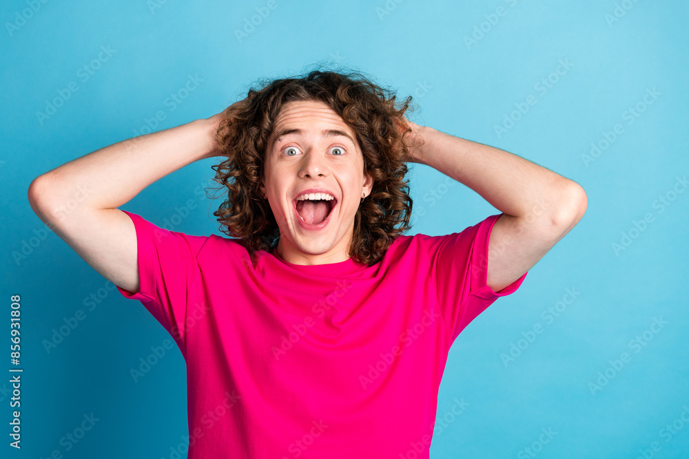 Photo of crazy ecstatic guy with wavy hairstyle earrings dressed pink shirt holding arms on head isolated on blue color background Photo of crazy ecstatic guy with wavy hairstyle earrings dressed pink shirt holding arms on head isolated on blue color background
