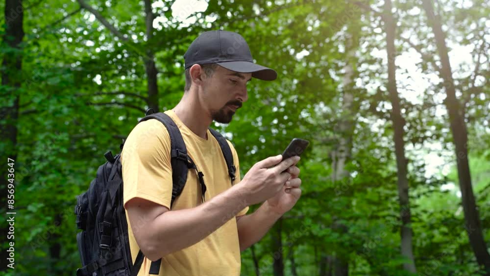 Face man with beard and backpack in forest uses phone to touch the screen looking for connection signal gps application orientation tourist travel hike lost sun communication telephone Face man with beard and backpack in forest uses phone to touch the screen looking for connection signal gps application orientation tourist travel hike lost sun communication telephone