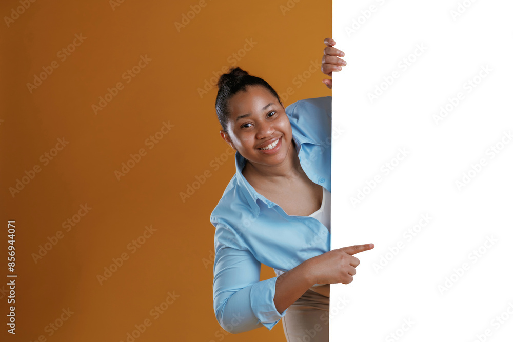 White copy space wall, hiding behind it. African American woman is in the studio against yellow background White copy space wall, hiding behind it. African American woman is in the studio against yellow background