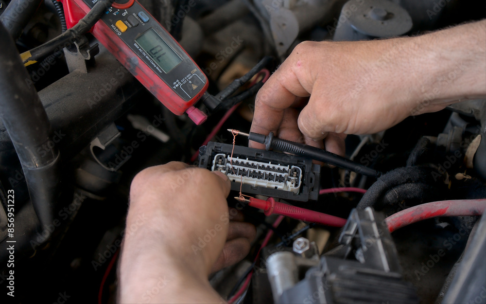 An auto electrician using a measuring device to check the voltage in a vehicle's electrical circuit, diagnosing wiring issues for repair. Auto service. An auto electrician using a measuring device to check the voltage in a vehicle's electrical circuit, diagnosing wiring issues for repair. Auto service.