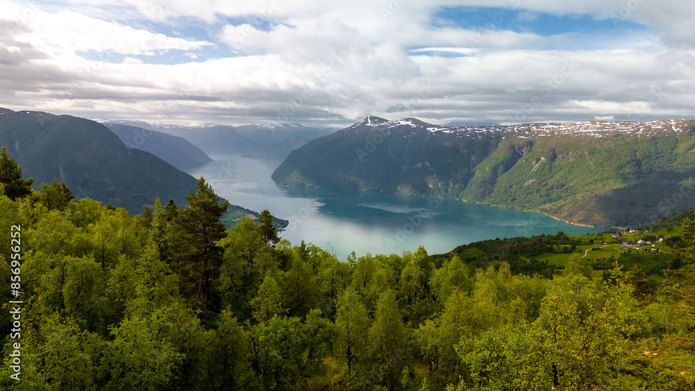 A breathtaking view of a Norwegian fjord, surrounded by lush green forests and snow-capped mountains, under a cloudy sky. Molden hike, Norway A breathtaking view of a Norwegian fjord, surrounded by lush green forests and snow-capped mountains, under a cloudy sky. Molden hike, Norway
