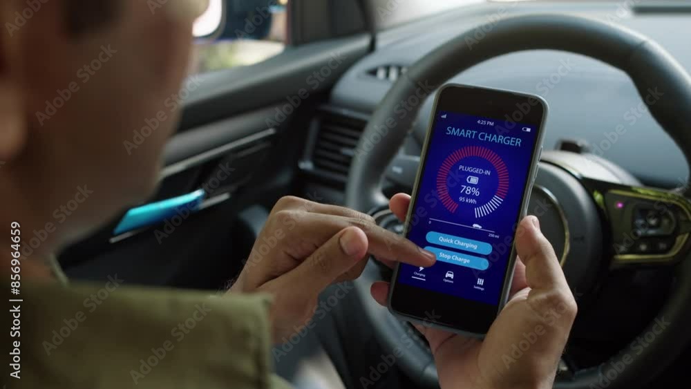 Over the shoulder view of male driver sitting in car and looking at smartphone with EV charging application on screen Over the shoulder view of male driver sitting in car and looking at smartphone with EV charging application on screen