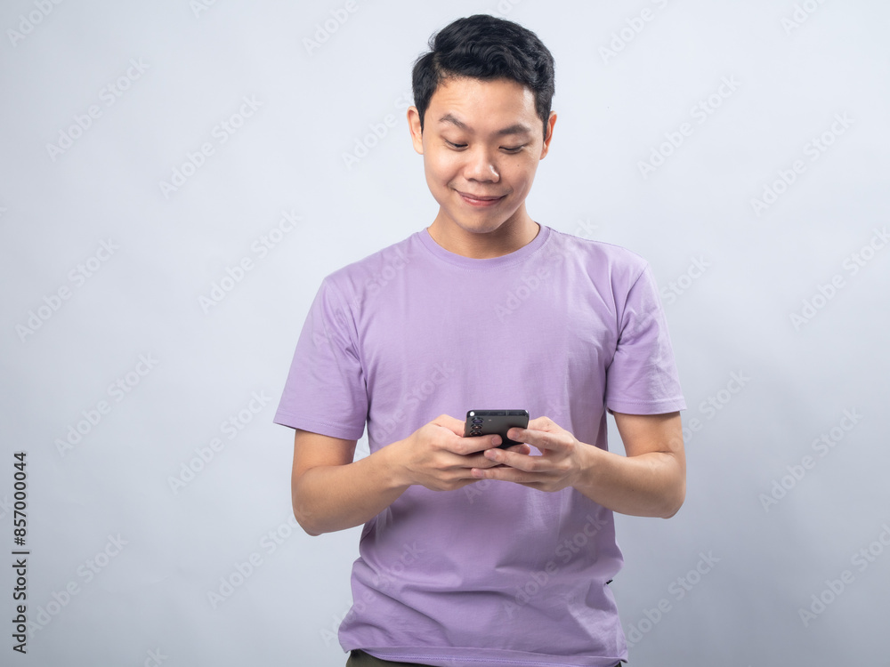 Young Asian man in a lavender t-shirt angrily shouting at his smartphone. Studio shot on a plain background, highlighting his frustration and casual fashion Young Asian man in a lavender t-shirt angrily shouting at his smartphone. Studio shot on a plain background, highlighting his frustration and casual fashion