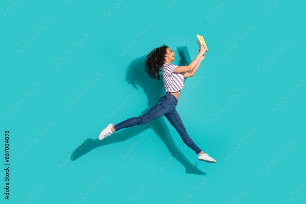 Full length photo of lovely young lady running jump read book dressed stylish striped garment isolated on cyan color background Full length photo of lovely young lady running jump read book dressed stylish striped garment isolated on cyan color background