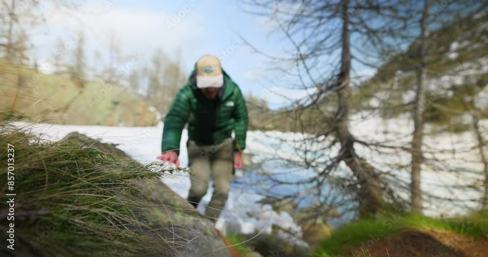 Slow motion hiker climbs up snow covered trail near mountain stream Slow motion hiker climbs up snow covered trail near mountain stream