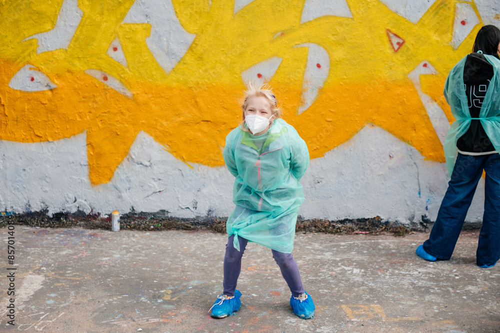 Obraz premium A person in a green protective suit and face mask standing in front of a graffiti-covered wall, symbolizing urban survival.