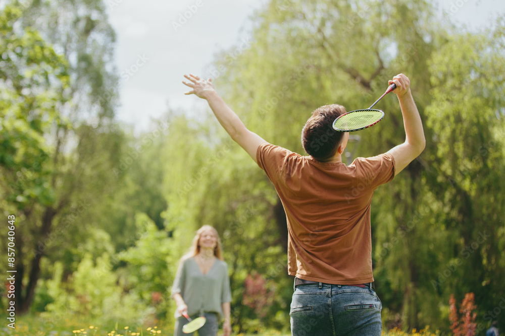 Fototapeta premium A young couple is playing badminton on a lawn in a park.