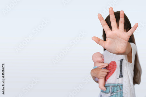 girl with her hand covering her face in a gesture of protest against violence and abuse. The child with scared doll covering his face, on white background.