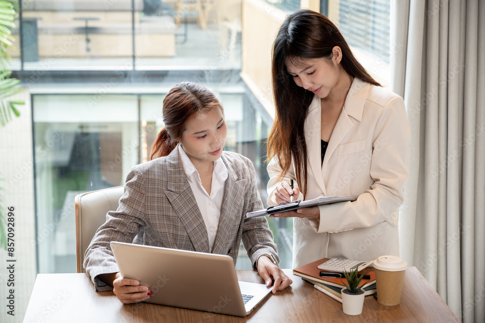 Two attractive Asian businesswomen or female office workers are checking the documents, having a meeting, discussing work, and working on an assignment together in the meeting room. Two attractive Asian businesswomen or female office workers are checking the documents, having a meeting, discussing work, and working on an assignment together in the meeting room.