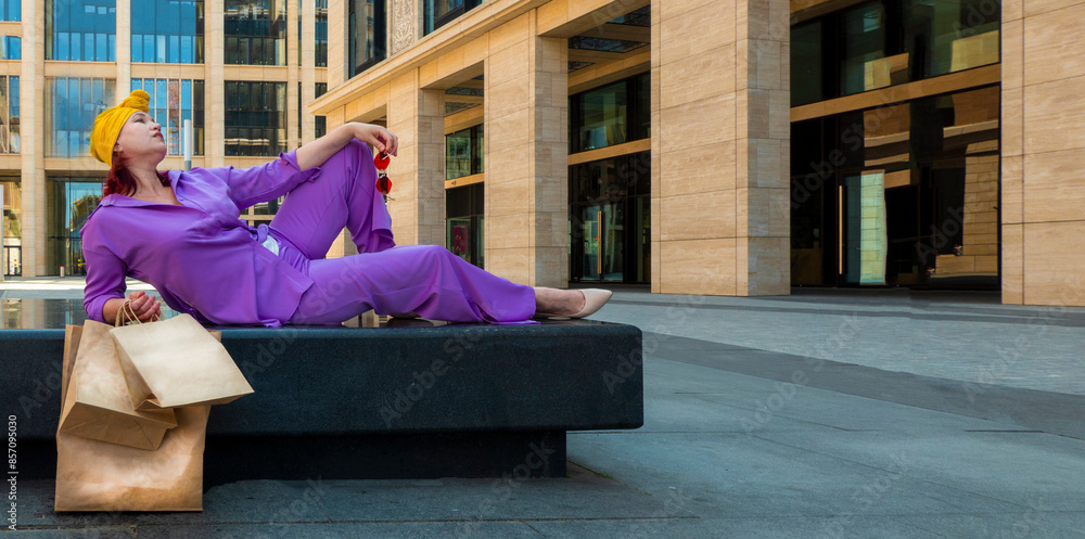 woman with craft shopping bags in the city. The concept of fashionable Consumerism and ecology. Adult Asian woman in a purple suit with red and yellow accents enjoys shopping. banner with copy space
