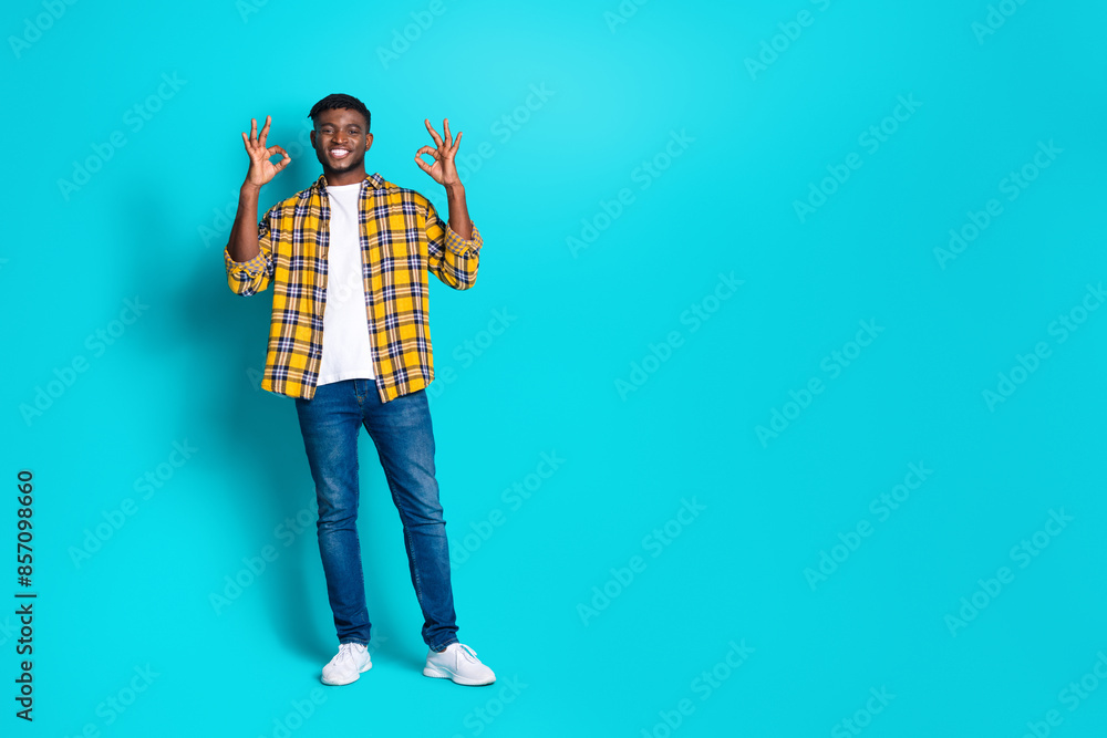 Photo of positive cheerful nice man wear trendy checkered clothes okey sign empty space isolated on cyan color background Photo of positive cheerful nice man wear trendy checkered clothes okey sign empty space isolated on cyan color background