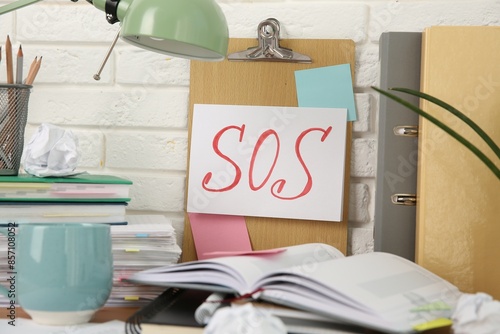 Note with word SOS and stationery on table at workplace