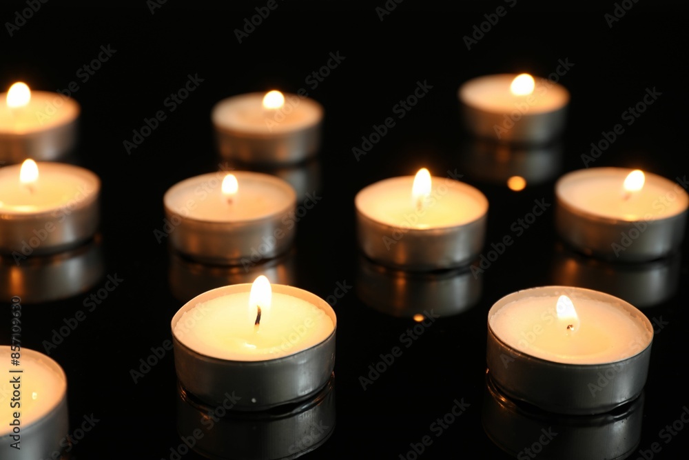 Many burning tealight candles on mirror surface against black background Many burning tealight candles on mirror surface against black background