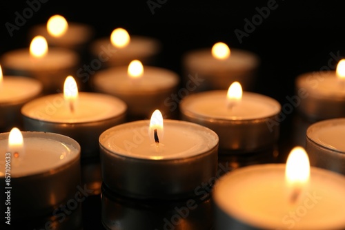 Many burning tealight candles on black background, closeup © New Africa