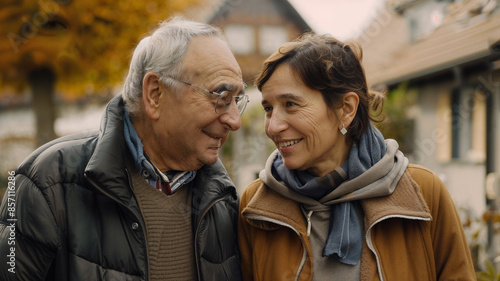 An elderly couple is seen sharing a warm, affectionate look while walking outdoors, dressed in winter clothing, showcasing love, companionship, and happiness during their walk.