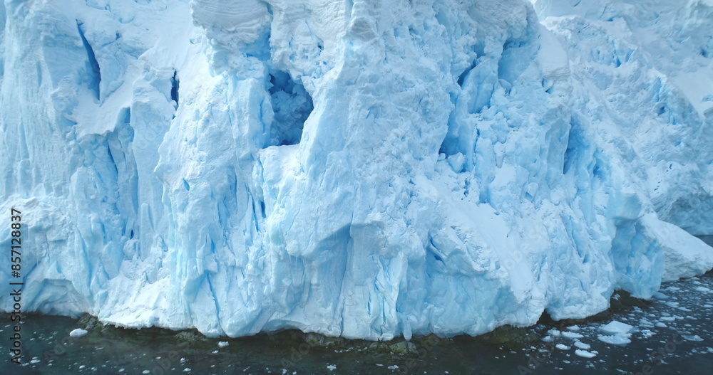 Obraz premium Giant glacier towering in Antarctica polar ocean. A huge iceberg ice wall formation float cold water, mountain slope in background. Winter landscape close up. Climate change at polar glacier landscape