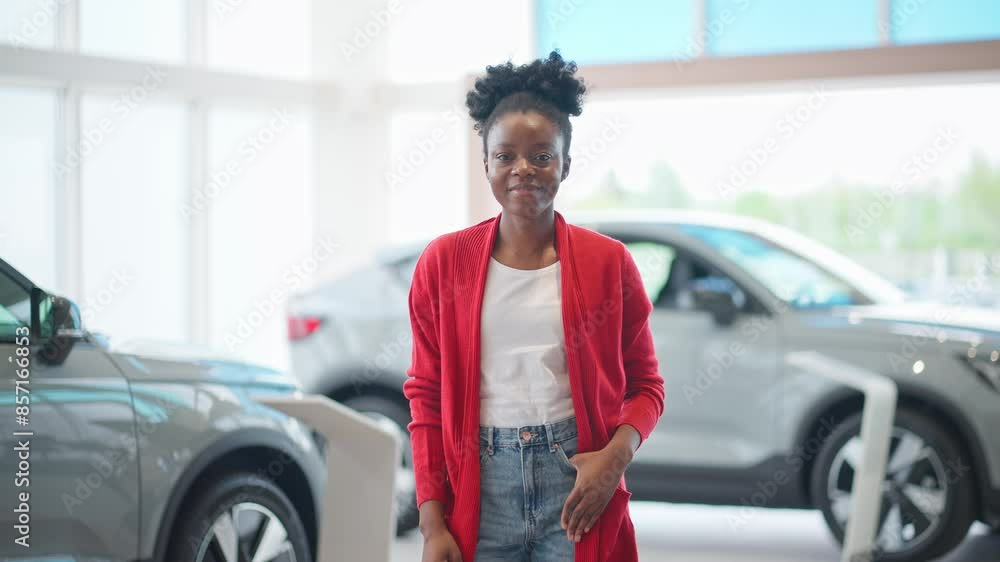 Charming African American woman in casual clothes standing in middle of auto agency. Cheerfully smiling with joy. Positively glancing directly at camera. Potential buyer visiting shop to choose car. Charming African American woman in casual clothes standing in middle of auto agency. Cheerfully smiling with joy. Positively glancing directly at camera. Potential buyer visiting shop to choose car.