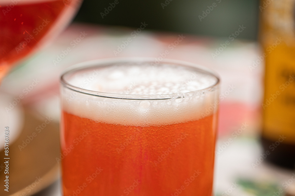 vista in primo piano di un bicchiere trasparente messo su un tavolo apparecchiato, riempito completamente con una bevanda dolce, gassata e frizzante di colore rosso vista in primo piano di un bicchiere trasparente messo su un tavolo apparecchiato, riempito completamente con una bevanda dolce, gassata e frizzante di colore rosso