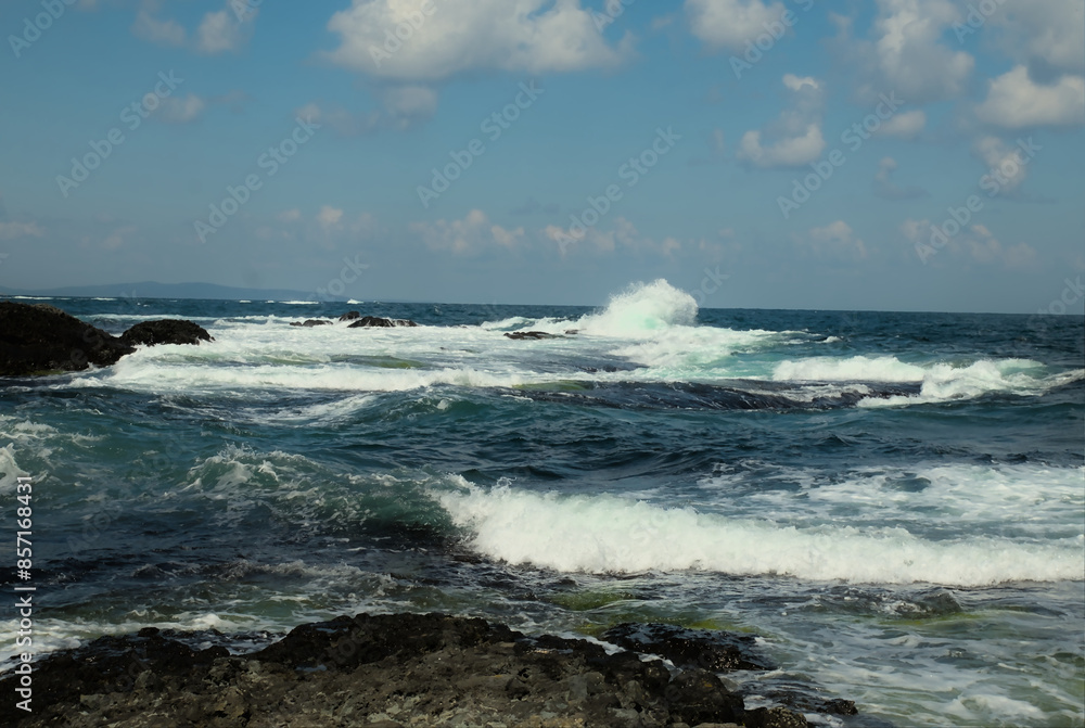 A stormy sea with waves rising and crashing against a rocky shore. Clear day with a blue sky. Background. A stormy sea with waves rising and crashing against a rocky shore. Clear day with a blue sky. Background.