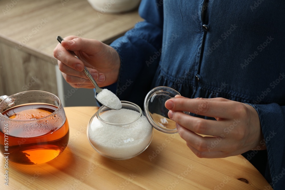 Woman adding sugar into aromatic tea at wooden table indoors, closeup Woman adding sugar into aromatic tea at wooden table indoors, closeup