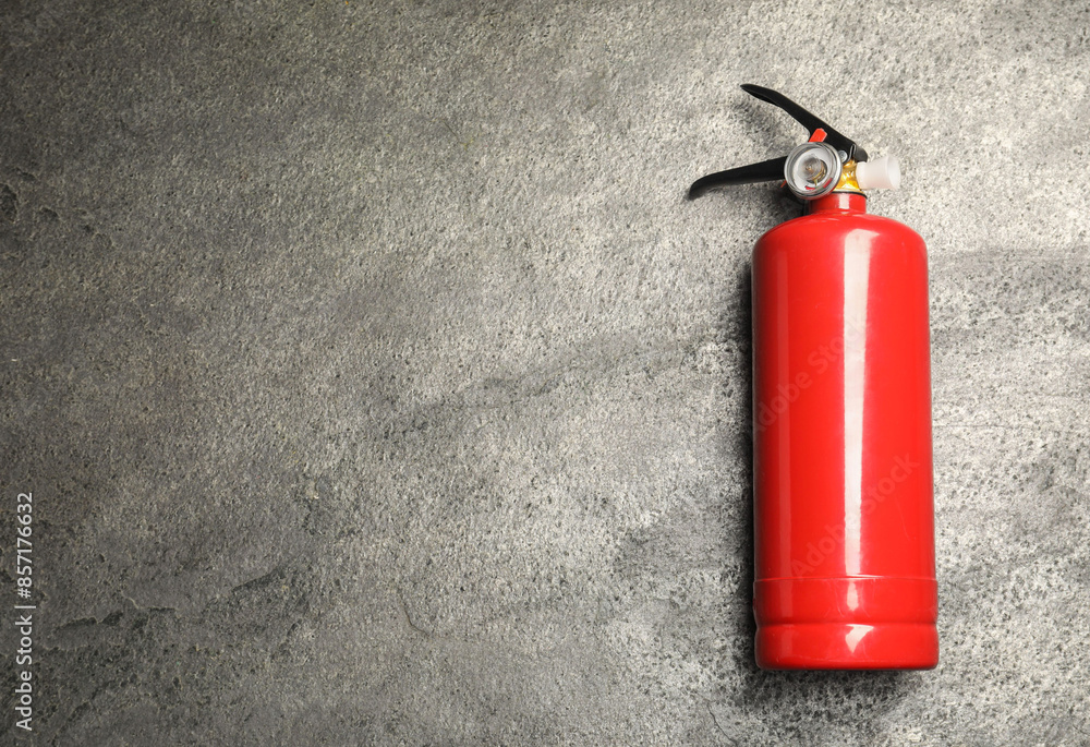 Fototapeta premium One red fire extinguisher on gray textured background, top view. Space for text