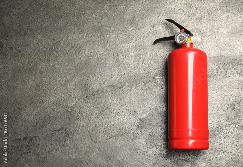 One red fire extinguisher on gray textured background, top view. Space for text