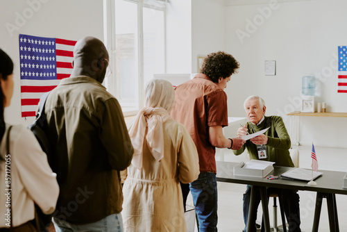 Group of ethnically diverse men and women standing in line to get ballot papers at voting station on election day