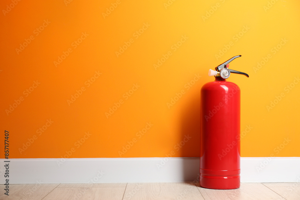 Obraz premium Fire extinguisher on floor near orange wall, space for text