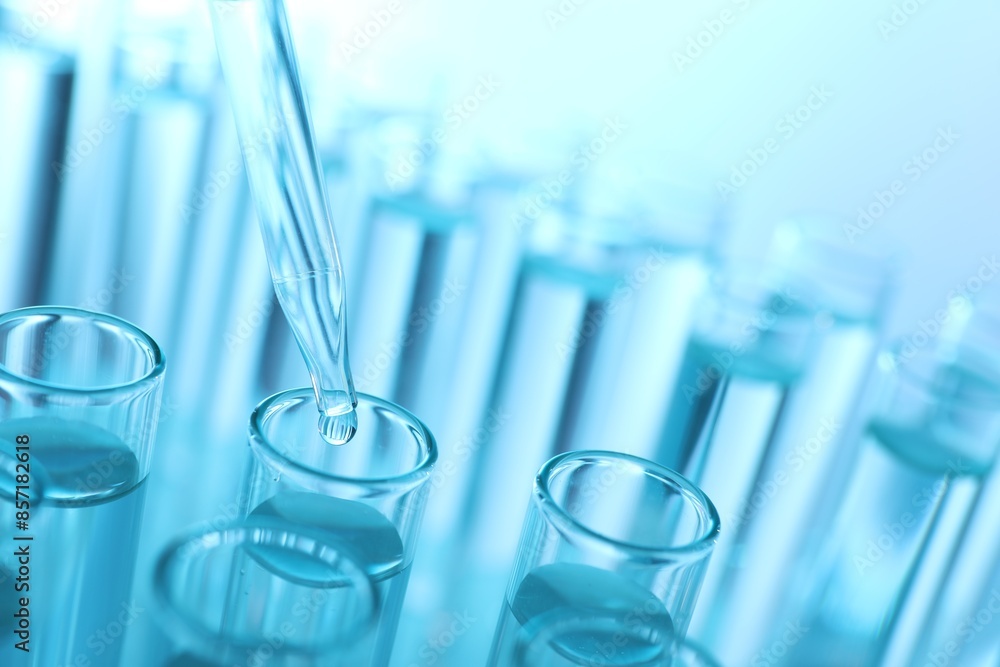Dripping liquid from pipette into test tube on light blue background, closeup Dripping liquid from pipette into test tube on light blue background, closeup
