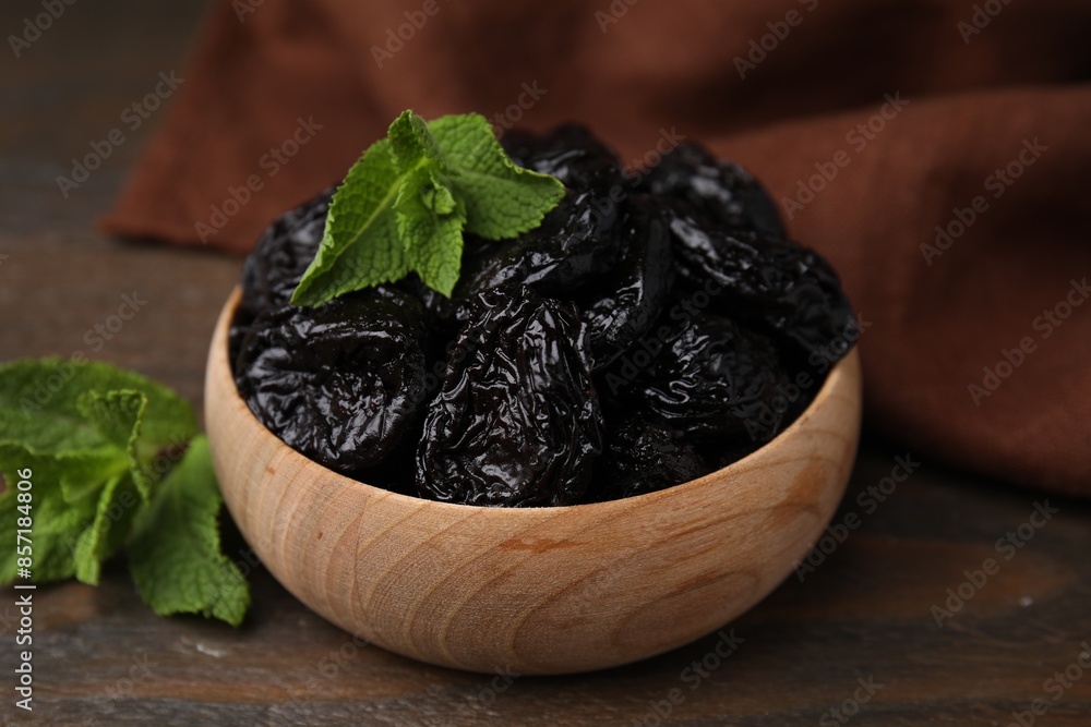 Tasty dried plums (prunes) and mint leaves in bowl on wooden table, closeup Tasty dried plums (prunes) and mint leaves in bowl on wooden table, closeup