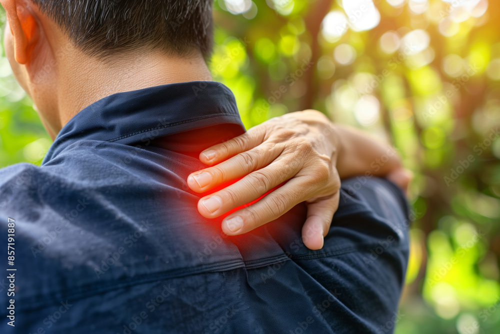 Fototapeta premium Man experiencing upper back pain outdoors on a sunny day